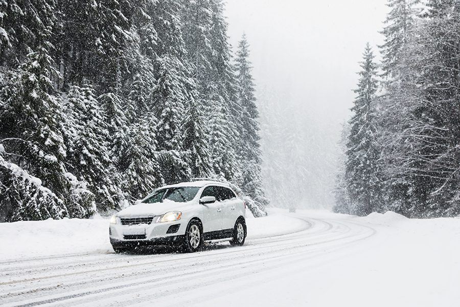A car drives on a snow-covered road in the forest