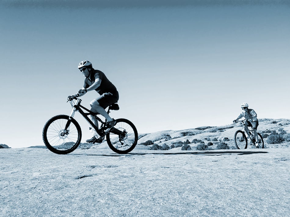  Two bicyclists ride their mountain bike in the desert.