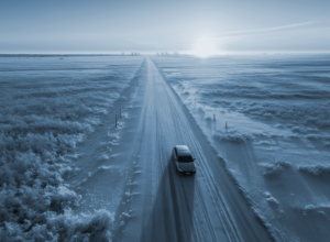 Car drives down a snowy country road with the sun on the horizon