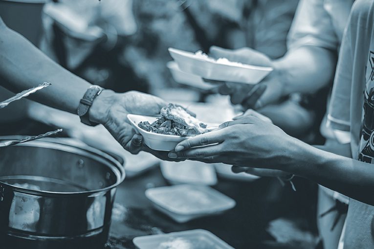 A volunteer hands a plate of food to another person