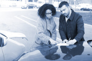 A man and a woman exchange insurance information on the hood of a car