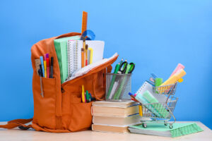Backpack filled with school supplies, books, scissors, and a small shopping cart nearby